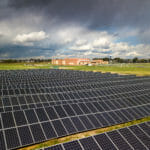 field of solar panels in front of a red brick high school with sun and dark clouds