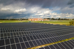 field of solar panels in front of a red brick high school with sun and dark clouds