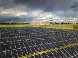 field of solar panels in front of a red brick high school with sun and dark clouds